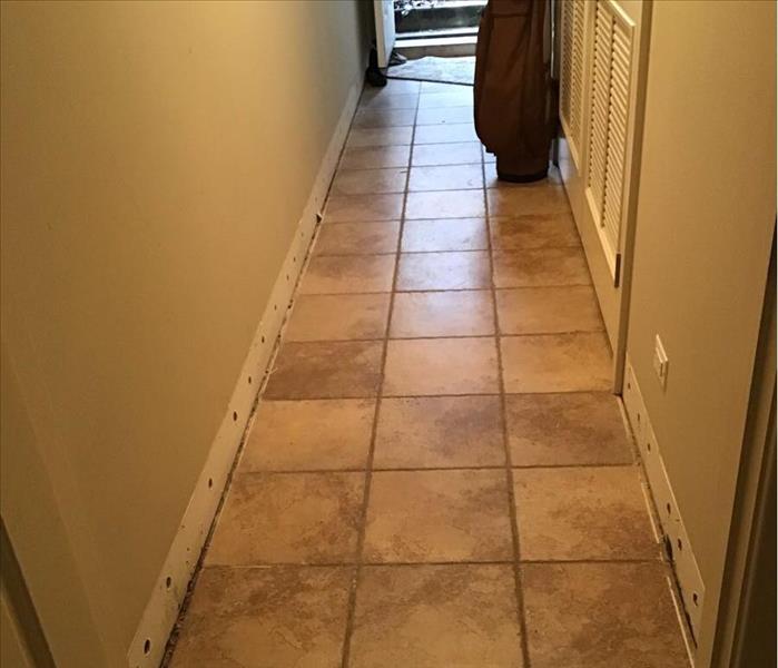 Dry brown tile in a hallway with trim removed and a stairway in the background.