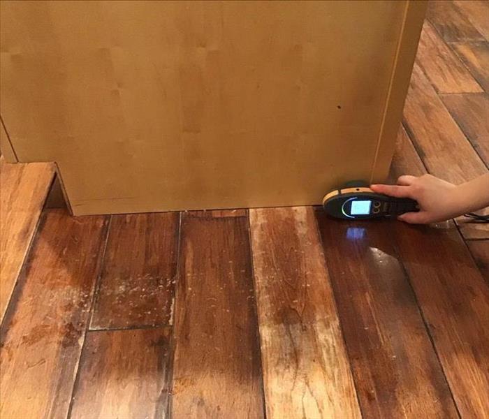 Wet hardwood floors with a moisture meter at the base of the cabinet.