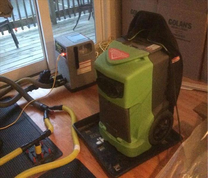 Green SERVPRO equipment drying out hardwood floors with yellow hoses on the floor.