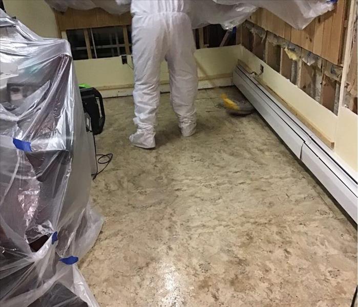 Muddy tile floor with a SERVPRO worker in a white suit with a mop.