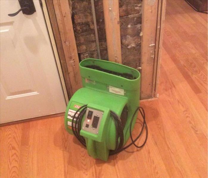 Green SERVPRO air mover on a hardwood floor with a white door in the background.