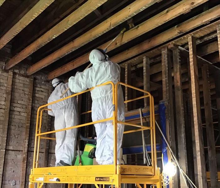 Two SERVPRO employees with white suits on a yellow ladder cleaning soot.