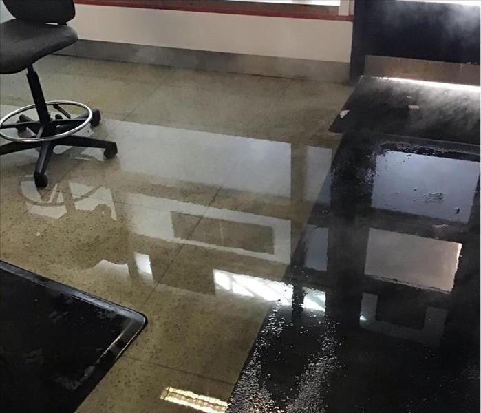 Wet tile floor of an office hallway with a chair in the background.