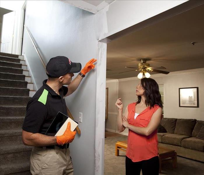 SERVPRO employee speaking to a customer at the bottom of a staircase next to a living room.