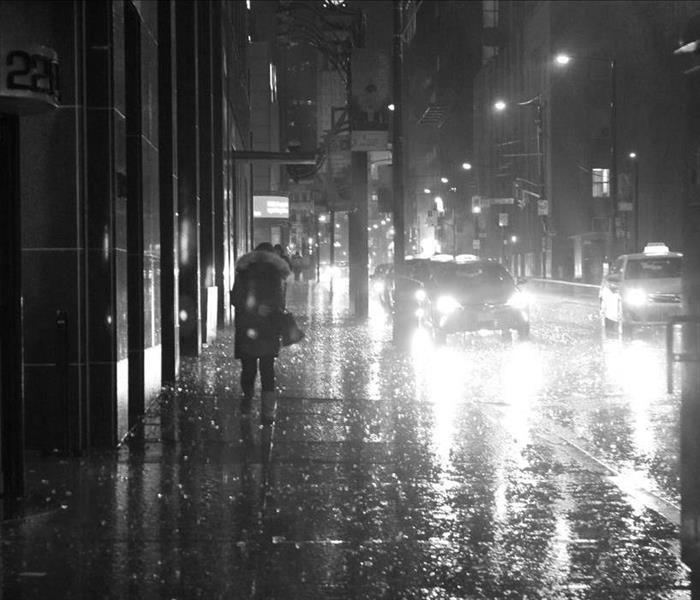 Rainy city street at night with people walking on the sidewalk and cars in the street.