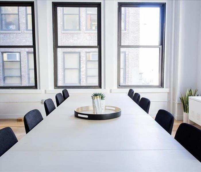 White conference table with black chairs in a room with 4 windows looking out.