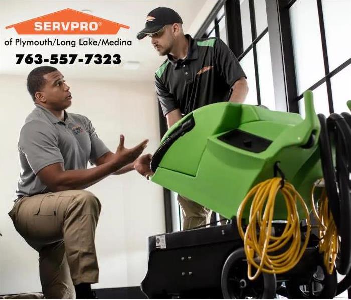 A green SERVPRO machine with two employees around it.